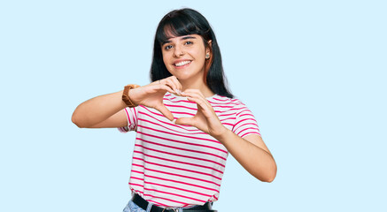 Young hispanic girl wearing casual clothes smiling in love doing heart symbol shape with hands. romantic concept.