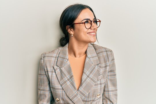 Young brunette woman wearing business jacket and glasses looking away to side with smile on face, natural expression. laughing confident.