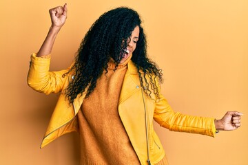Middle age african american woman wearing wool winter sweater and leather jacket dancing happy and cheerful, smiling moving casual and confident listening to music