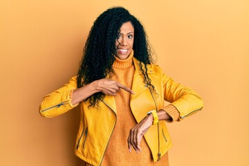 Middle age african american woman wearing wool winter sweater and leather jacket in hurry pointing to watch time, impatience, upset and angry for deadline delay