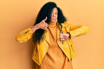 Middle age african american woman wearing wool winter sweater and leather jacket doing thumbs up and down, disagreement and agreement expression. crazy conflict