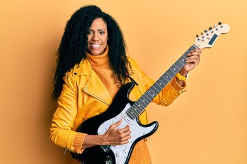 Middle age african american woman playing electric guitar smiling with a happy and cool smile on face. showing teeth.