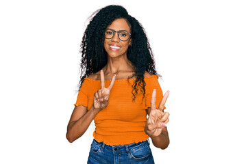 Middle age african american woman wearing casual clothes and glasses smiling looking to the camera showing fingers doing victory sign. number two.