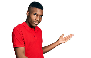 Young african american man wearing casual red t shirt inviting to enter smiling natural with open hand