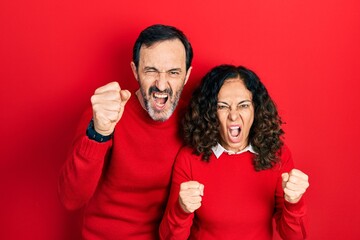 Middle age couple of hispanic woman and man hugging and standing together angry and mad raising fists frustrated and furious while shouting with anger. rage and aggressive concept.