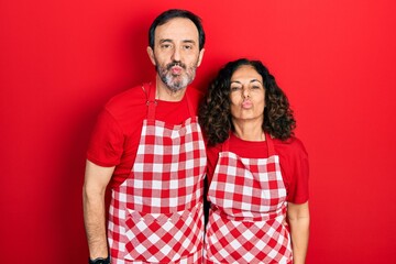 Middle age couple of hispanic woman and man wearing cook apron looking at the camera blowing a kiss on air being lovely and sexy. love expression.