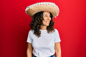 Middle age hispanic woman holding mexican hat looking away to side with smile on face, natural expression. laughing confident.