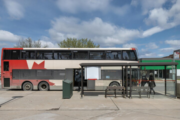 Bus stop in the city daytime with passengers embarking and disembarking double decker bus, glass bus stop in foreground