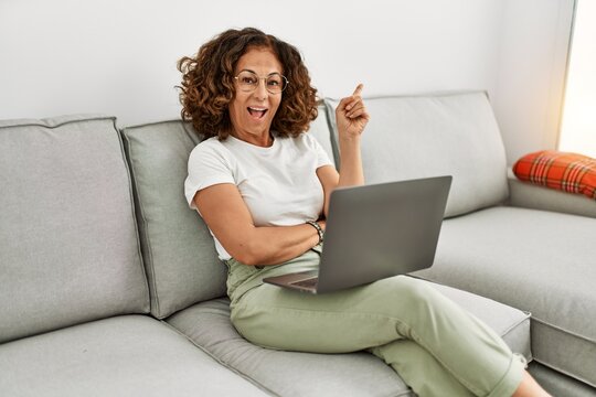 Middle age hispanic woman working using computer laptop at home smiling happy pointing with hand and finger to the side