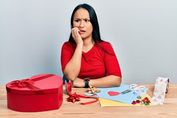 Beautiful hispanic woman with nose piercing doing handcraft creative decoration looking stressed and nervous with hands on mouth biting nails. anxiety problem.