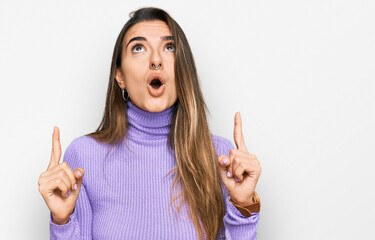 Young hispanic woman wearing casual clothes amazed and surprised looking up and pointing with fingers and raised arms.