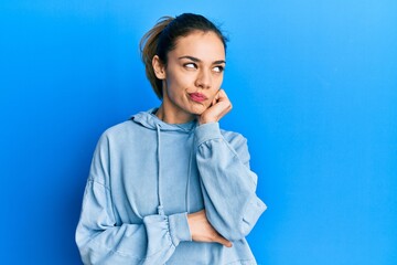 Young caucasian blonde woman wearing casual sweatshirt thinking concentrated about doubt with finger on chin and looking up wondering