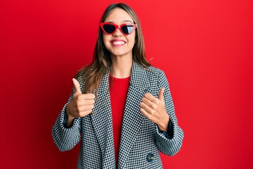 Young brunette woman wearing fashion and modern look success sign doing positive gesture with hand, thumbs up smiling and happy. cheerful expression and winner gesture.