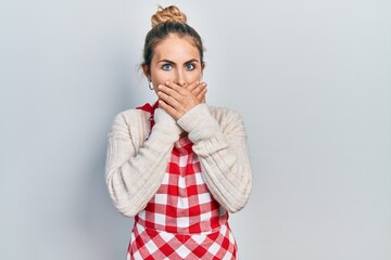 Beautiful caucasian woman with blond hair wearing apron shocked covering mouth with hands for mistake. secret concept.