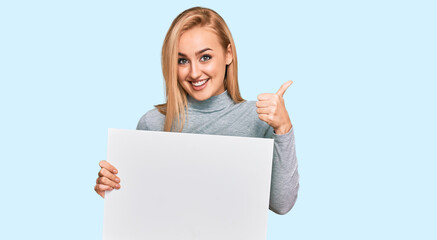 Fototapeta premium Beautiful caucasian woman holding blank empty banner smiling happy and positive, thumb up doing excellent and approval sign