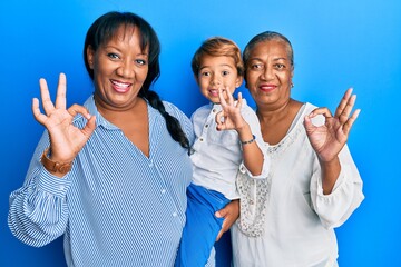 Hispanic family of grandmother, mother and son hugging together doing ok sign with fingers, smiling...