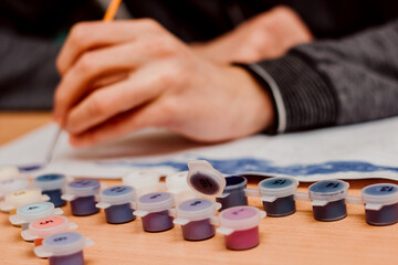 Fototapeta premium The guy paints a picture by numbers. Watercolor paints. Painting brush, Painting by numbers concept
