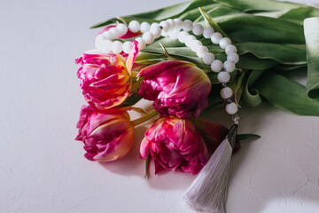Bouquet of pink tulips and rosary on a white background. hard light