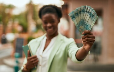 Young african american businesswoman smiling happy holding brazilian real banknotes at the city