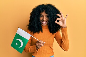 African american woman with afro hair holding pakistan flag doing ok sign with fingers, smiling friendly gesturing excellent symbol