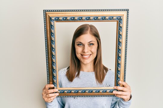 Beautiful caucasian woman holding empty frame smiling with a happy and cool smile on face. showing teeth.