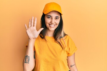 Young hispanic woman wearing delivery uniform and cap showing and pointing up with fingers number five while smiling confident and happy.