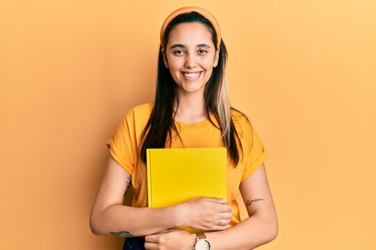 Young hispanic woman wearing student backpack and holding book smiling with a happy and cool smile on face. showing teeth.