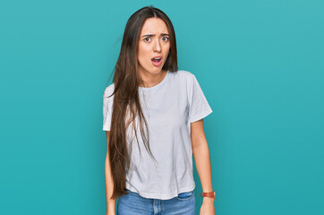 Young hispanic girl wearing casual white t shirt in shock face, looking skeptical and sarcastic, surprised with open mouth