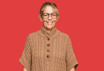 Middle age blonde woman wearing sweater and glasses looking positive and happy standing and smiling with a confident smile showing teeth