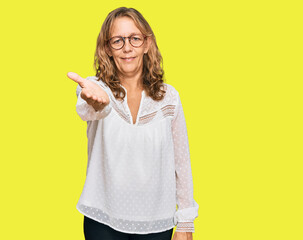 Middle age blonde woman wearing casual white shirt and glasses smiling friendly offering handshake as greeting and welcoming. successful business.