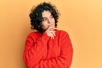 Fototapeta na wymiar Young hispanic woman with curly hair wearing casual winter sweater with hand on chin thinking about question, pensive expression. smiling with thoughtful face. doubt concept.