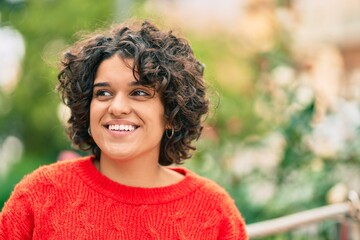 Young hispanic woman smiling happy looking to the side at the park.