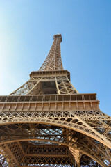 Front view of the Eiffel tower seen from beneath in Paris, blue sky, sunny day, warm tones and almost no clouds