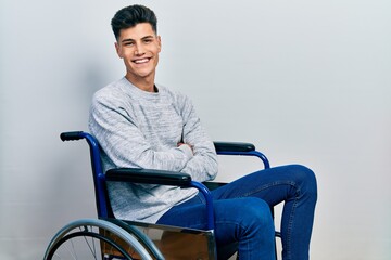 Young hispanic man sitting on wheelchair happy face smiling with crossed arms looking at the...