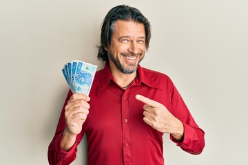 Middle age handsome man holding 50 polish zloty banknotes smiling happy pointing with hand and...
