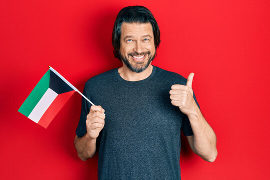 Middle age caucasian man holding kuwait flag smiling happy and positive, thumb up doing excellent and approval sign
