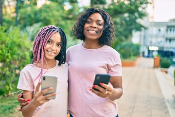 African american mother and daugther hugging and using smartphone at the park.