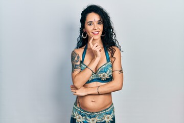 Young woman wearing bindi and traditional belly dance clothes looking confident at the camera smiling with crossed arms and hand raised on chin. thinking positive.