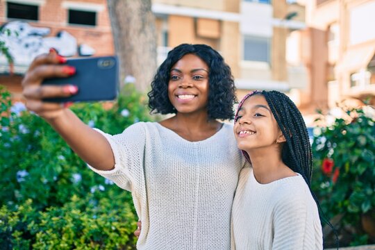 African american mother and daugther hugging and making selfie by the smartphone at the park.