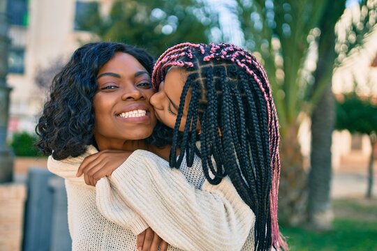 Beautiful african american mother giving daughter piggyback ride and kissing at the park.