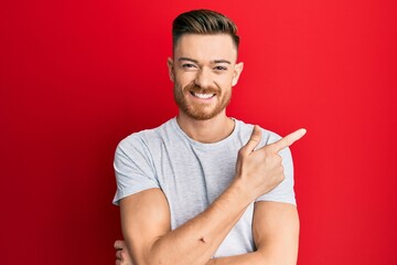 Young redhead man wearing casual grey t shirt smiling cheerful pointing with hand and finger up to the side