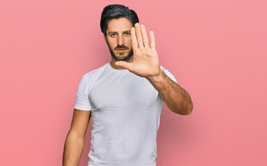 Young hispanic man wearing casual white t shirt doing stop sing with palm of the hand. warning expression with negative and serious gesture on the face.