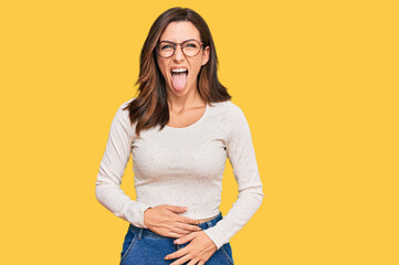 Young brunette woman wearing casual clothes and glasses sticking tongue out happy with funny...