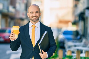 Young hispanic bald businessman holding binder drinking coffee at the city.