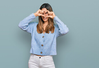 Young woman wearing casual clothes doing heart shape with hand and fingers smiling looking through sign