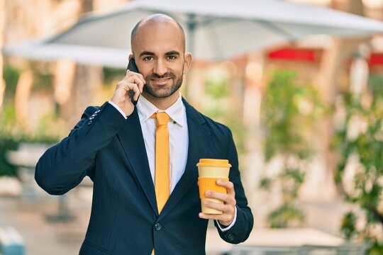 Young hispanic bald businessman talking on the smartphone drinking coffee at the city.