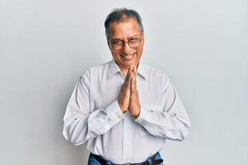 Middle age indian man wearing casual clothes and glasses praying with hands together asking for forgiveness smiling confident.