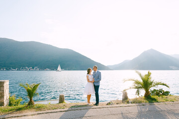 Fototapeta na wymiar Groom holds the hands of bride on the coast against the background of the mountains of the city of Perast in Montenegro