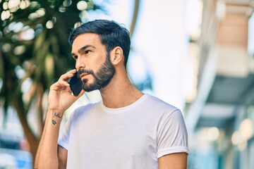 Young hispanic man with serious expression talking on the smartphone at the city.