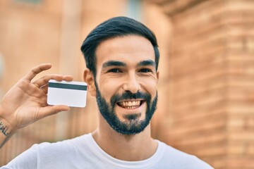 Young hispanic man smiling happy holding credit card at the city.